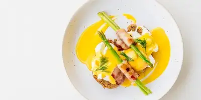 Uova alla Benedict su asparagi con pancetta e salsa olandese