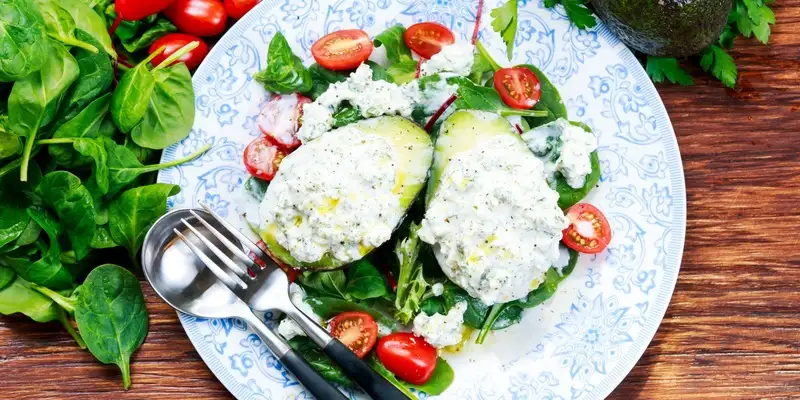Insalata di avocado e pomodori con puntini di formaggio cremoso e pinoli